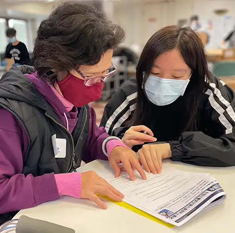 Photo of a younger woman assisting an older woman with completing documents.