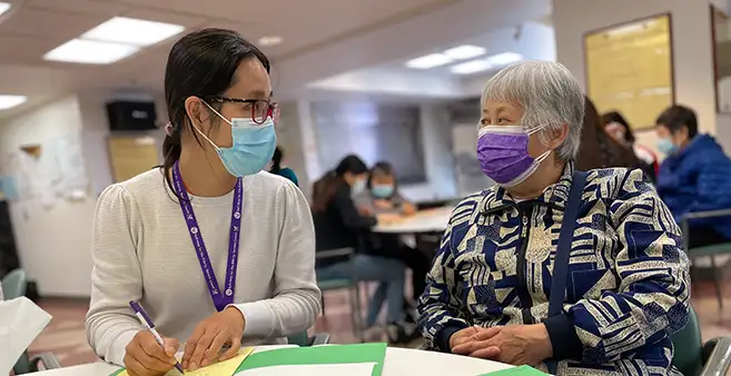 Photo of a younger woman assisting an older woman with completing documents.